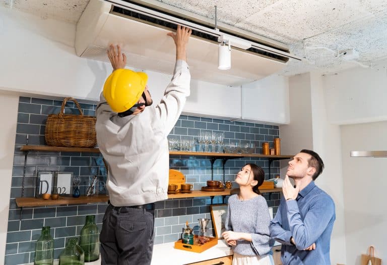 Handyman wearing a helmet while he is working on the AC unit. Customers watch the process