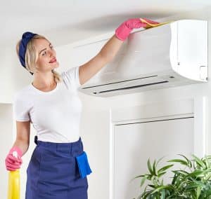 Women in white and blue with a blue bandanna and pink gloves cleaning AC unit