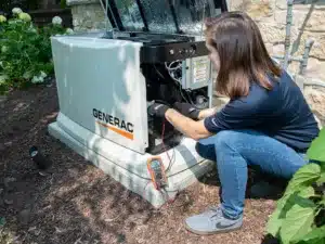 A person repairs a GENERAC generator outdoors, using tools and a digital multimeter.