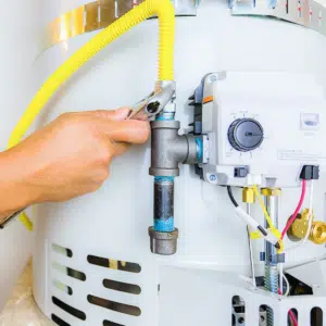 Close-up of a person using a wrench to tighten a gas line on a water heater.